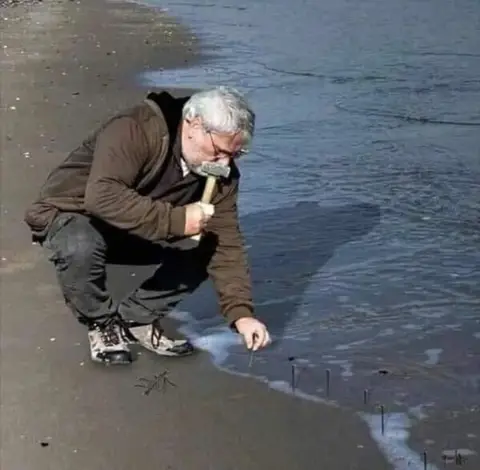 Guy Hammering Nails Into Sand